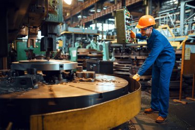 Üniformalı ve kasklı Turner büyük torna ve fabrikada çalışıyor. Endüstriyel üretim, metal mühendisliği, güç makineleri üretimi
