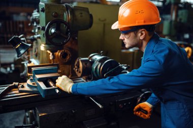 Worker in uniform and helmet works on lathe, plant. Industrial production, metalwork engineering, power machines manufacturing clipart
