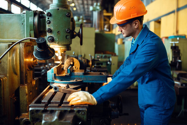 Turner in uniform and helmet works on lathe, plant. Industrial production, metalwork engineering, power machines manufacturing
