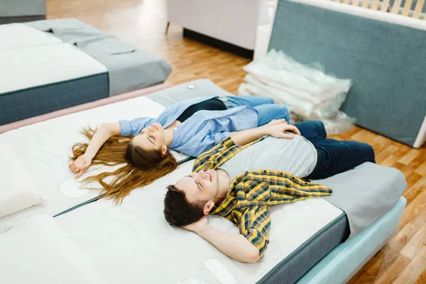年轻夫妇躺在家具商店陈列室的床上 男人和女人在商店里寻找卧室的样品 丈夫和妻子为现代住宅的内部购买商品 — 图库照片