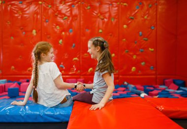 Jouful kız arkadaşları eğlence merkezinde yumuşak küplerin arasında oynuyorlar. Tatildeki kızlar, çocukluk mutluluğu, çocuk parkındaki mutlu çocuklar.