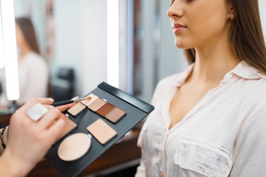 Kozmetikçi kozmetik mağazasında bir kadının yüzüne gölgeler koyar. Lüks güzellik salonu, moda pazarında kadın müşteri ve güzellik uzmanı.