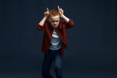 Küçük çocuk stüdyoda surat asıyor. Mutlu çocukluk, eğlenen çocuklar, karanlık arka planda izole edilmiş komik çocuklar, çocuk duyguları.