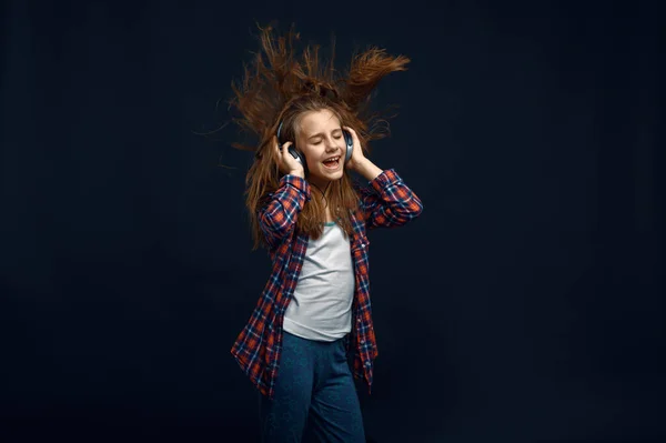 スタジオで強力な気流に対してヘッドフォンで女の子 髪の効果を開発 子供と風暗い背景に隔離された子供の感情 — ストック写真