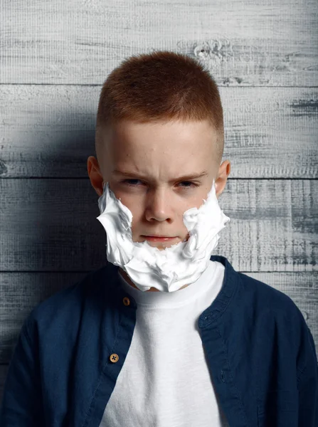 一个严肃的小男孩在工作室刮胡子泡沫的脸上 因木制背景 儿童情绪 学童照片而被隔离的儿童 — 图库照片