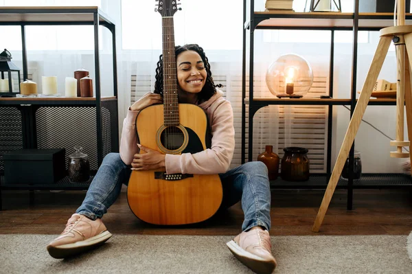 床に座って 家でギターを抱きしめる陽気な女性 楽器を持つ美しい女性が部屋でリラックス 女性音楽愛好家休息 — ストック写真