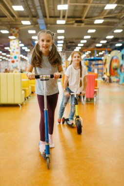 Küçük kız arkadaşlar eğlence merkezinde scooterlara biniyor. Bayan çocuklar tatilde, çocukluk mutluluğunda, çocuk parkında mutlu çocuklar.