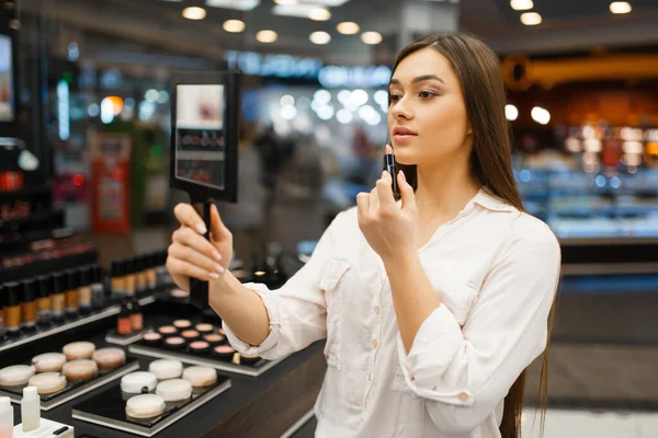 迷人的女人带着镜子在化妆品商店涂口红 奢侈品美容店橱窗里的买家 时尚市场上的女性顾客 — 图库照片