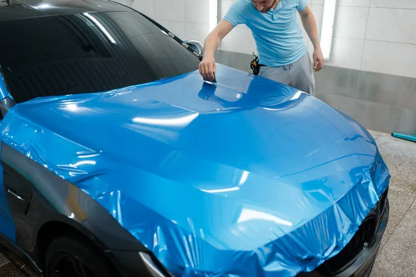 汽车包装 带刮板的人在车盖上安装保护膜或乙烯箔 工人们做自动详细说明 汽车油漆保护层 专业调音 — 图库照片