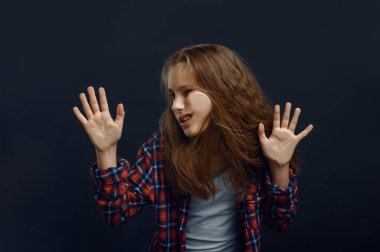 Küçük kız yüzünü stüdyoda cama yaslıyor. Mutlu çocukluk, eğlenen çocuklar, karanlık arka planda izole edilmiş komik çocuklar.