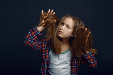 Küçük hanım yüzünü stüdyoda cama yaslıyor. Mutlu çocukluk, eğlenen çocuklar, karanlık arka planda izole edilmiş tatlı çocuklar, çocuk duyguları.