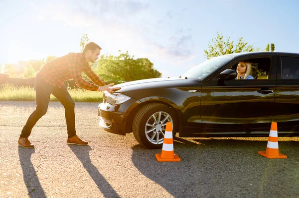 Female student passes between cones, lesson in driving school. Man teaching lady to drive vehicle. Drivers license education