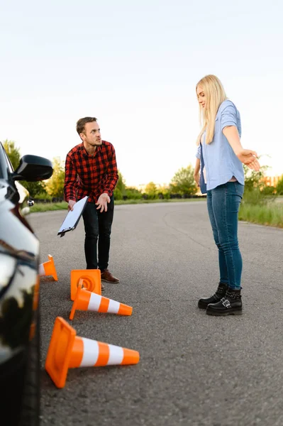 Sad female student in car and instructor, all traffic cones are downed, lesson in driving school. Man teaching lady to drive vehicle. Drivers license education