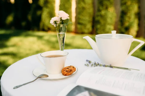 テーブルセッティング お菓子とロマンチックなティーパーティー 屋外の白いテーブルクロス 食器に豪華な銀食器 夏の牧草地での結婚式 — ストック写真