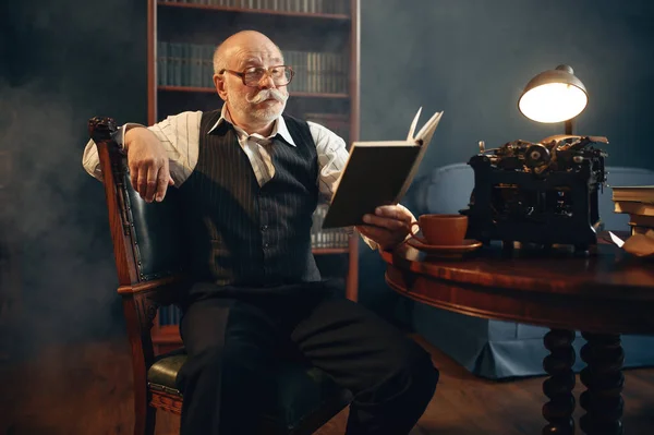필자는 사무실에서 빈티지 타자기로 작품을 읽는다 안경쓴 노인이 연기와 영감을 — 스톡 사진