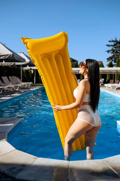 Slim woman with inflatable mattress at the poolside on resort. Beautiful girl relax at the pool in sunny day, summer holidays of attractive female person