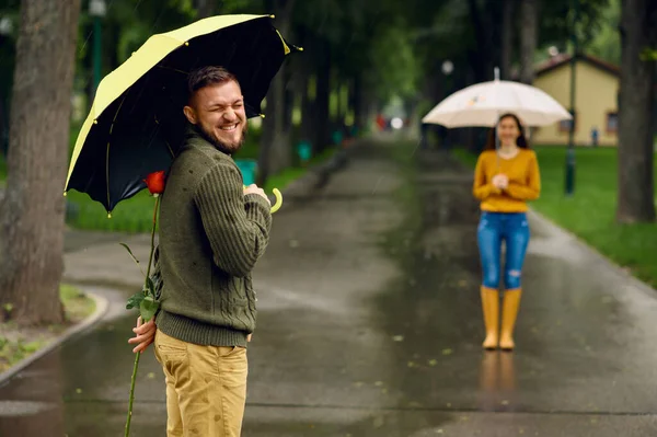 雨の日 公園で傘を持つ愛のカップル 赤いバラの男は歩く道で彼の女性を待っている 路地で雨の多い天気 — ストック写真