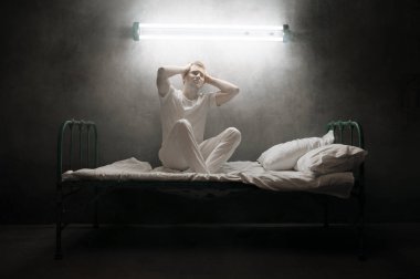 Yatakta oturan psikopat adam, arka planda karanlık oda. Psikedelik kişilik her gece sorun yaşıyor, depresyon ve stres, üzüntü, psikiyatri hastanesi