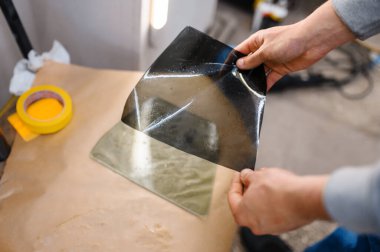 Erkek işçinin elinde araba boyama ve akort hizmeti var. Tamirci garajdaki araba camına vinil boya sürüyor, renkli otomobil camları.