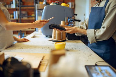 Kahvede erkek barista, siparişi bayan müşteri ödüyor. Adam kafeteryada taze espresso yapıyor, garson ve kadın barda tezgahta.