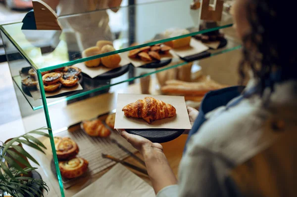 エプロンの女性バリスタは カフェのショーケースからクロワッサンを取ります カフェテリアでお菓子を選ぶ女性 バーのカウンターでウェイター — ストック写真