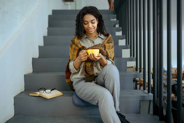 図書館カフェの階段にコーヒーを片手に笑顔の女子学生 カップを持つ女性は 教育と知識に本や眼鏡を開いた キャンパスで勉強する女の子 — ストック写真
