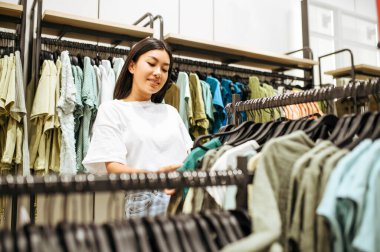 Elbise mağazasında kıyafet seçen bir kadın. Moda mağazasında alışveriş yapan bir kadın, giysilere bakan bir müşteri.