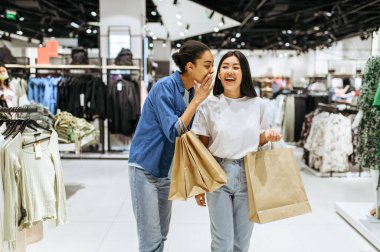 Çantalarında, giyim mağazasında alışveriş yapan mutlu kız arkadaşlar. Moda mağazasında alışveriş yapan kadınlar, alışveriş meraklıları.