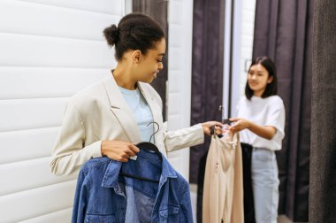 Soyunma odasında gülümseyen kızlar, giyim mağazası. Moda mağazasında alışveriş yapan kadınlar, alışveriş meraklıları, kıyafet deneyen müşteriler.