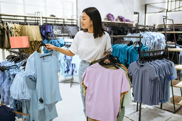 年轻妇女在服装店把衣服挂在衣架上 在时尚精品店购物的女性 购物狂 看衣服的购物者 — 图库照片