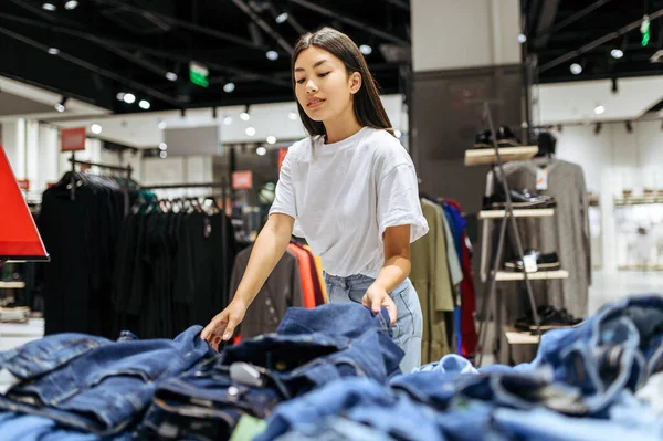 快乐的女人在服装店里选择牛仔裤 在时尚精品店购物的女性 购物狂 看衣服的购物者 — 图库照片