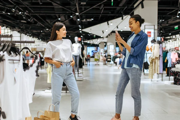Karton çantalı gülümseyen kız arkadaşlar giyim mağazasında yürür. Moda mağazasında alışveriş yapan kadınlar, alışverişçiler.
