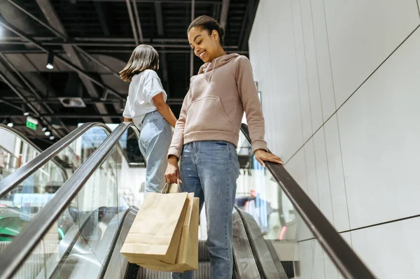 在自动扶梯 服装店买购物袋的快乐女孩 妇女在时尚精品店 购物狂 购物中心购物 — 图库照片