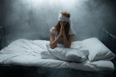 Gözleri bağlı deli bir kadın yatakta, arka planda karanlık bir odada oturuyor. Psikopat kadın her gece sorun yaşıyor. Depresyon, stres, üzüntü, psikiyatri hastanesi.