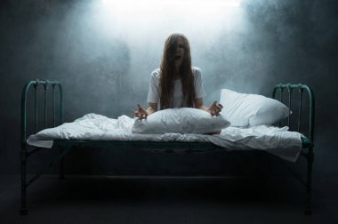 Psikopat kadın yatakta çığlık atıyor, uykusuzluk korkusu, arka planda karanlık dumanlı oda. Psikedelik kişilik her gece sorun yaşıyor, depresyon ve stres, üzüntü, psikiyatri hastanesi