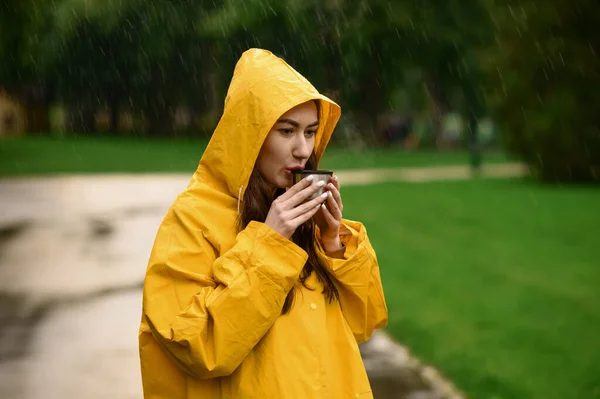 レインコートの女性は 夏の公園 雨の日に熱いお茶を飲む 散歩道に雨の岬に一人の女性だけで 路地で雨の日 — ストック写真