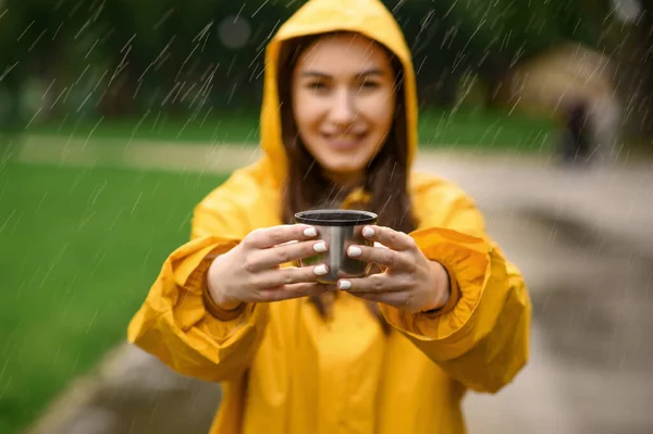 レインコートの女性は熱いお茶のカップを保持し 雨の日に夏の公園は ドロップを介して表示します 散歩道に雨の岬に一人の女性だけで 路地で雨の日 — ストック写真