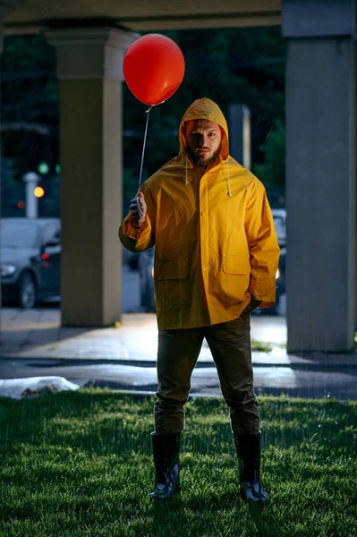 雨天带着气球在夏夜公园散步的可怕男人 穿着雨衣和橡胶靴的奇怪男人 巷子里的潮湿天气 — 图库照片