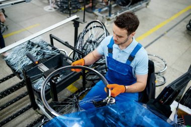 Makine aletli işçiler fabrikaya yeni bisiklet telleri kuruyor. Bisiklet tekerlekleri atölyede toplanıyor