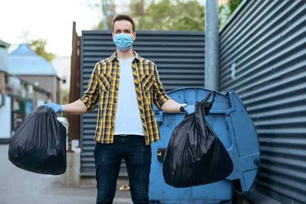 Volunteer in mask holds plastic trash bags outdoors, volunteering. People cleans city streets, ecological restoration, garbage collection and recycling, ecology care, environment cleaning