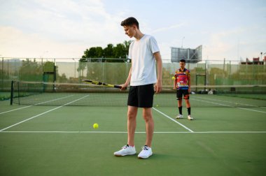 Male tennis players with rackets hits the balls, training on outdoor court. Active healthy lifestyle, people play sport game, fitness workout with racquets clipart
