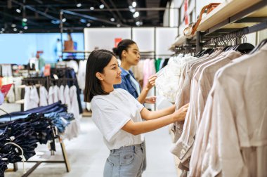 Elbise mağazasında kıyafet seçen iki kız arkadaş. Moda mağazasında alışveriş yapan kadınlar, alışveriş meraklıları, askılarda elbise arayanlar.