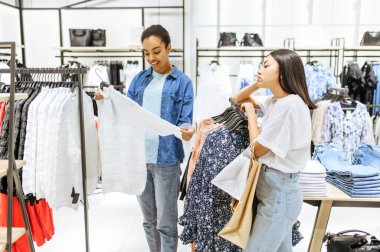 Giysi mağazasında pantolon seçen iki kız. Moda mağazasında alışveriş yapan kadınlar, alışveriş meraklıları, askılarda elbise arayanlar.