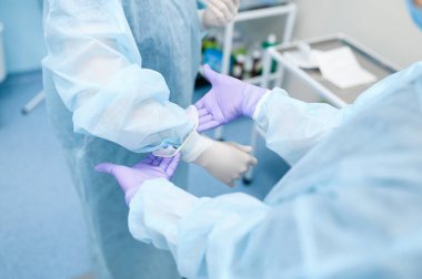 Kadın cerrah ve asistan ameliyathanede eldiven giyip ameliyata hazırlanıyorlar. Üniformalı doktor, klinik çalışanı, ilaç ve sağlık, hastanede sağlık hizmetleri