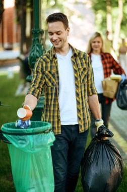 Genç adam çöpü parktaki plastik torbaya koyup gönüllü oluyor. Erkek kişi ormanı temizler, ekolojik restorasyon, ekolojik yaşam tarzı, çöp toplama ve geri dönüşüm, ekoloji bakımı, çevre temizliği