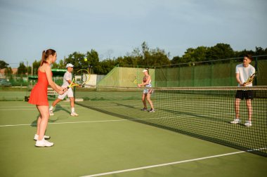 Karışık çiftler tenis antrenmanı, açık hava sahası. Aktif sağlıklı yaşam tarzı, insanlar raket ve topla spor oyunu oynar, raketlerle spor yapar.