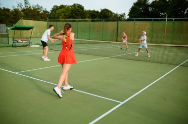 Karışık tenis oyuncuları, açık hava kortu. Aktif sağlıklı yaşam tarzı, insanlar raket ve topla spor oyunu oynuyor, fitness egzersizi.