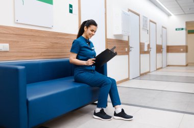 Klinikteki kanepede oturan defterli kadın cerrah, ameliyat. Üniformalı doktor, sağlık görevlisi, ilaç ve sağlık, hastanede profesyonel sağlık hizmetleri