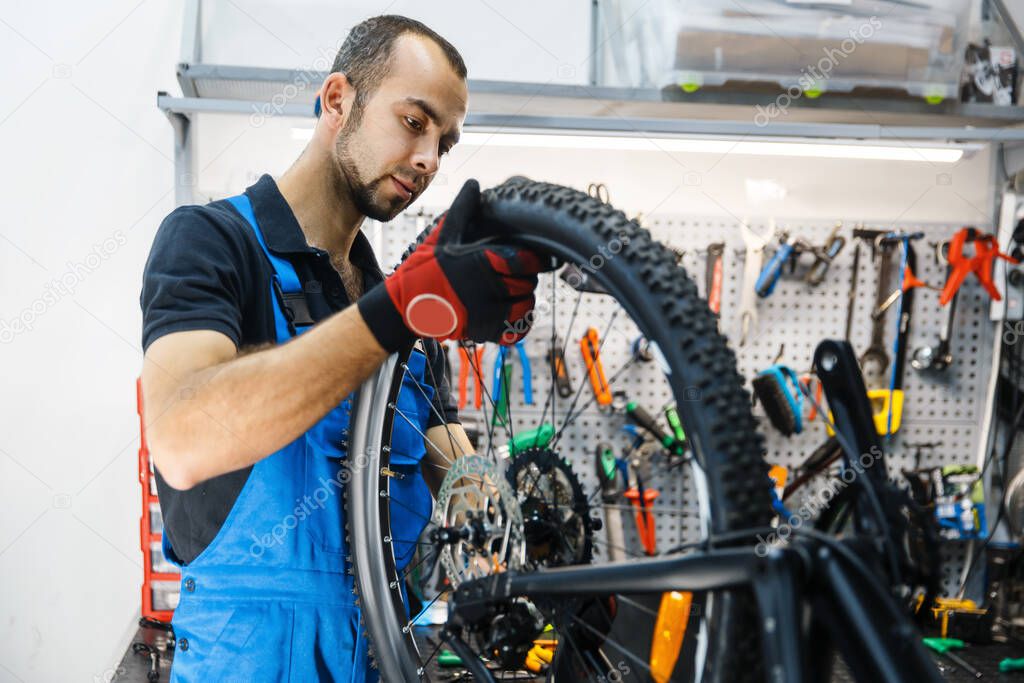 Bicycle assembly in workshop, man installs rear wheel. Mechanic in uniform fix problems with cycle, professional bike repairing service