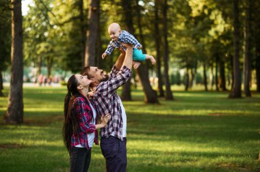 Anne, baba ve küçük bebek yaz parkında yürüyor. Anne, baba ve erkek çocuk çimlerde, çocukla piknik ormanda ekoseyle, aile mutluluğu